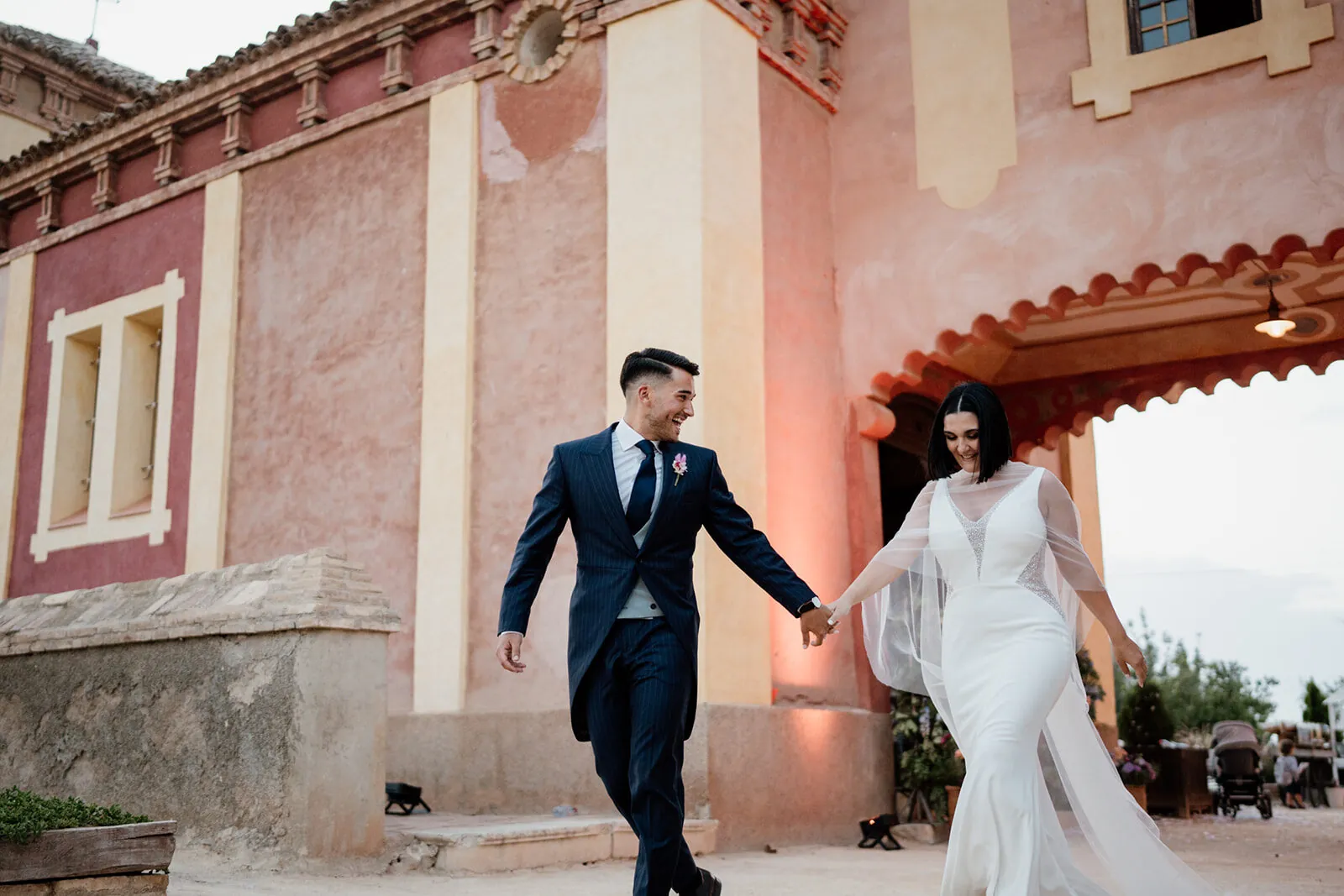 Los novios caminan frente a la hacienda de fachada rosa