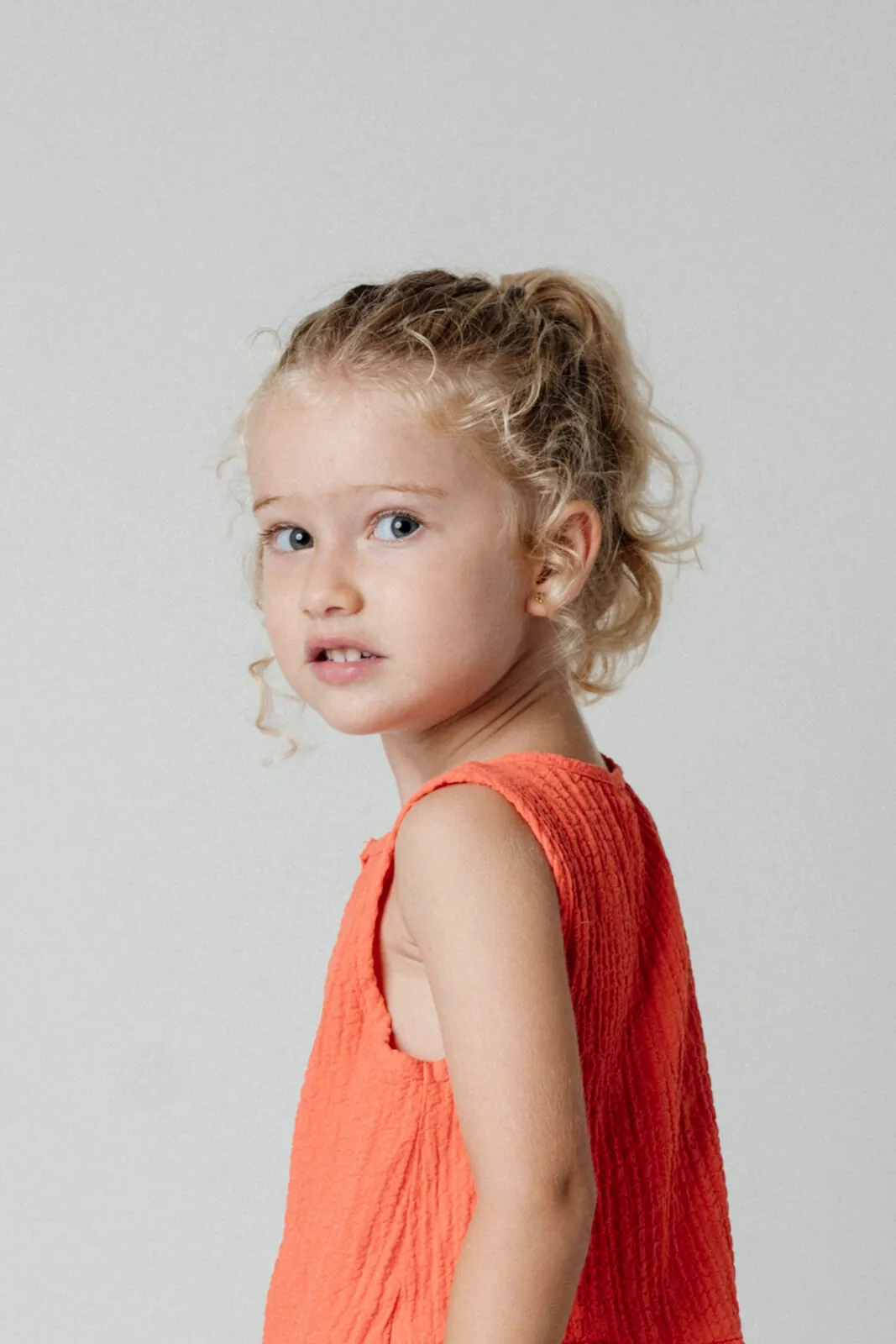 Retrato de estudio de una niña con vestido naranja sobre fondo claro